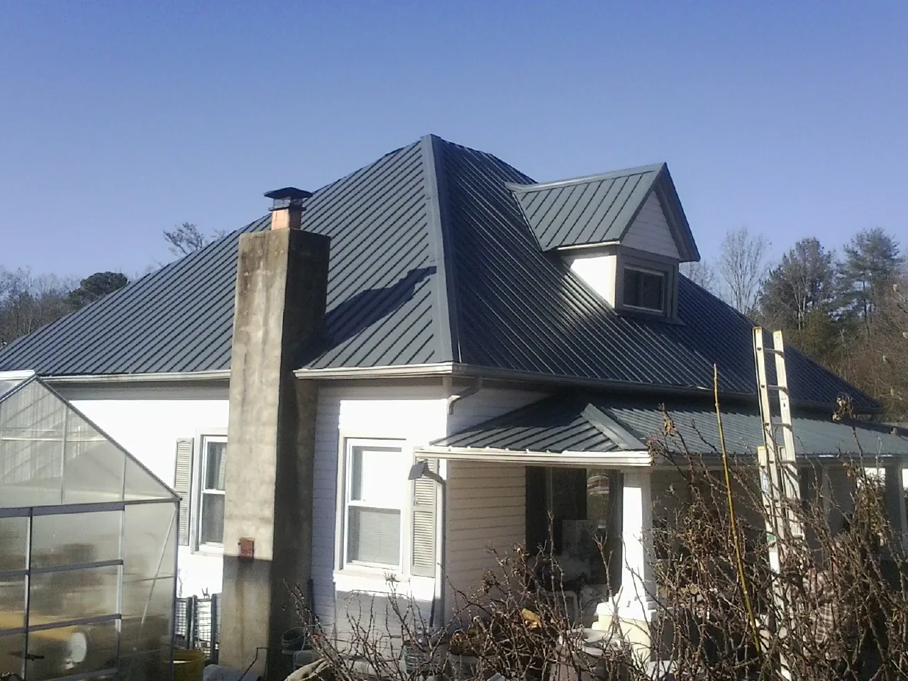 Dark blue standing seam metal roof on a white farmhouse with dormer — Slate & Tile Roof Repair by Roofing Brothers in Cherokee