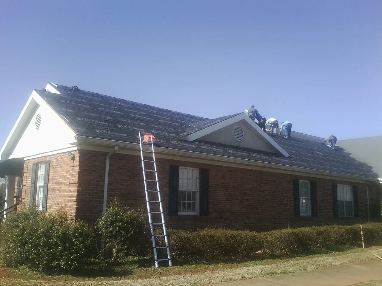 Crew tearing shingles off a brick ranch roof with a ladder set — Metal Roof Repair work by our crew in Cherokee