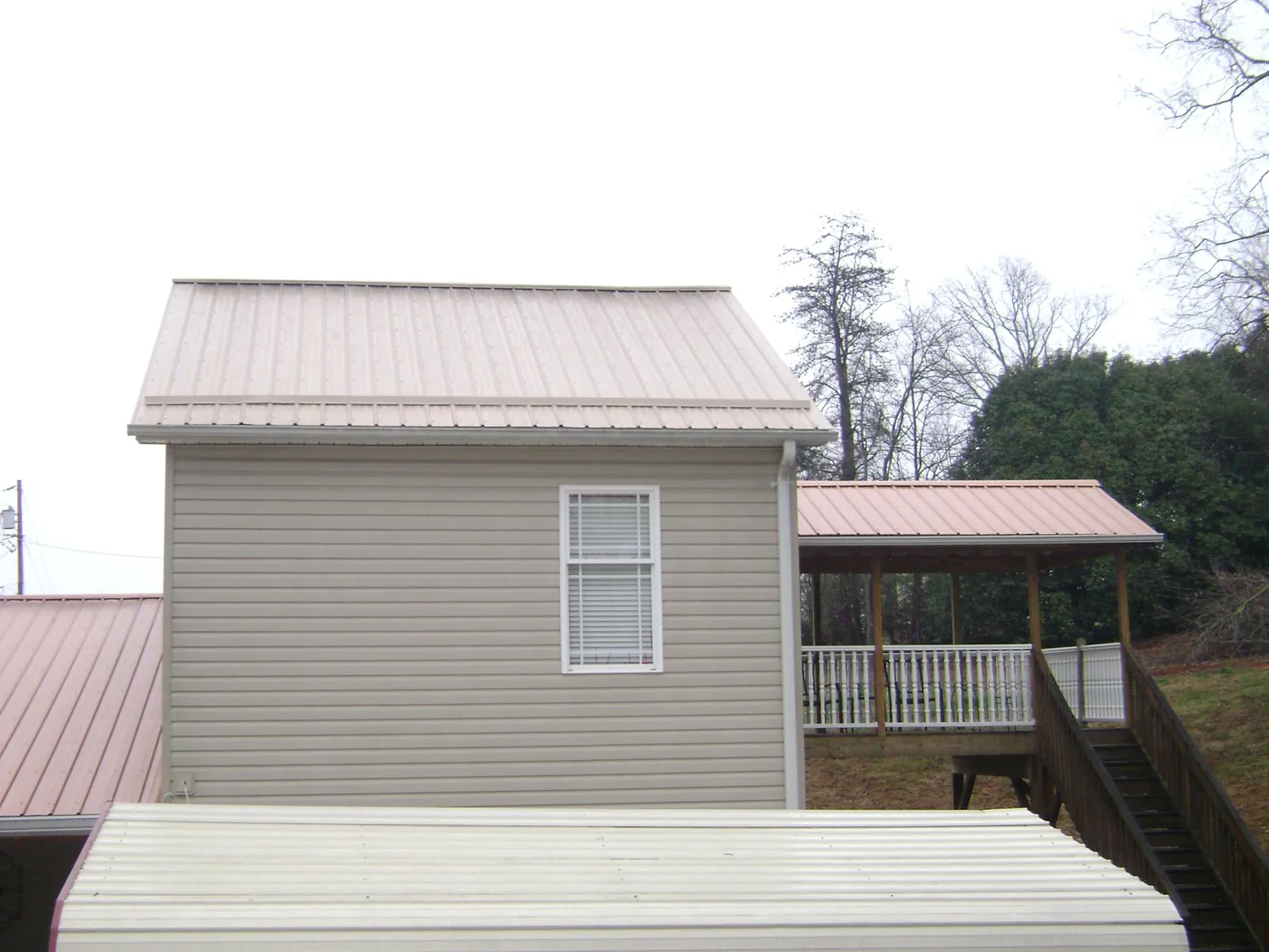 Tan metal roofs on a two story addition and attached porch, from a Roof Replacement job in Cherokee